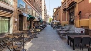 Une rue étroite bordée de terrasses et de tables, entourée d’immeubles aux devantures de magasins variées.