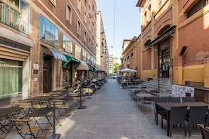 A narrow street with outdoor seating and tables, surrounded by buildings with various storefronts. - San Gervasio Apartment by Wonderful Italy (Bologna)