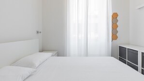 Une chambre à coucher comprenant un lit, une table de chevet, une commode et une fenêtre avec des rideaux légers.