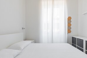 A bedroom with a bed, a nightstand, a dresser, and a window with sheer curtains. - San Gervasio Apartment by Wonderful Italy (Bologna)