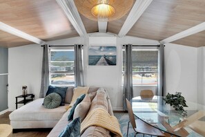 Ein modernes Wohnzimmer mit einer Couch, einem Glastisch und Blick auf das Meer durch große Fenster.