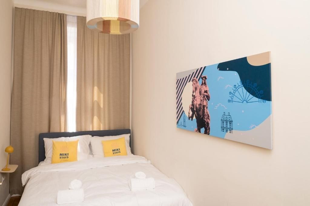 Une chambre d’hôtel avec un lit, une œuvre d’art accrochée au mur et une fenêtre avec des rideaux.