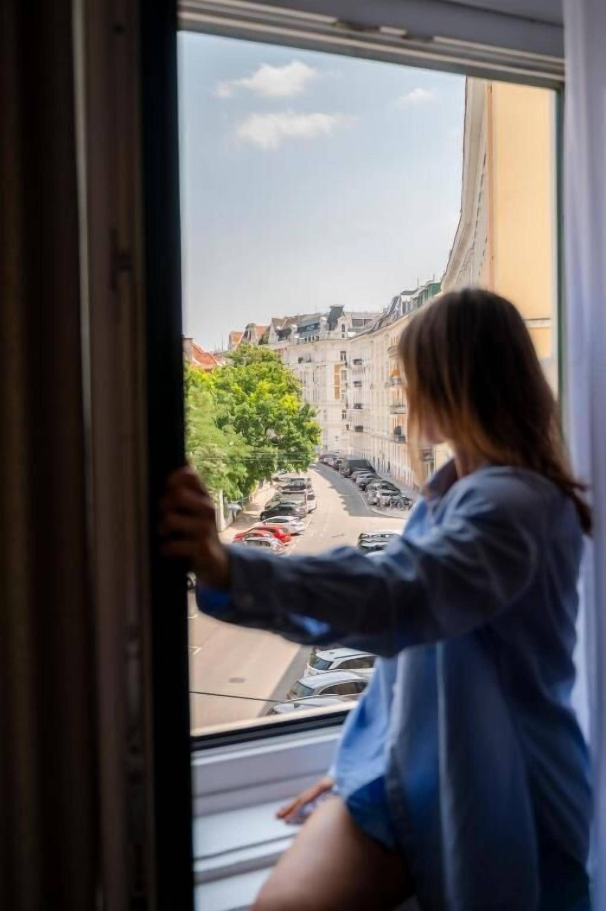 A person leaning on a window sill, looking out at a street view.