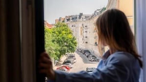 A person leaning on a window sill, looking out at a street view.