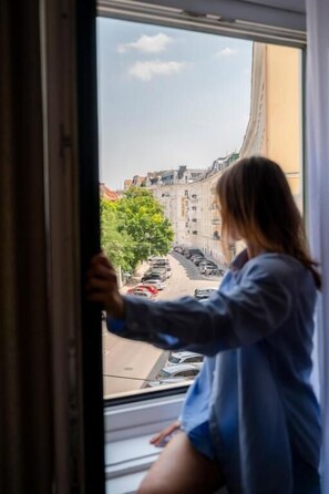 A person leaning on a window sill, looking out at a street view.