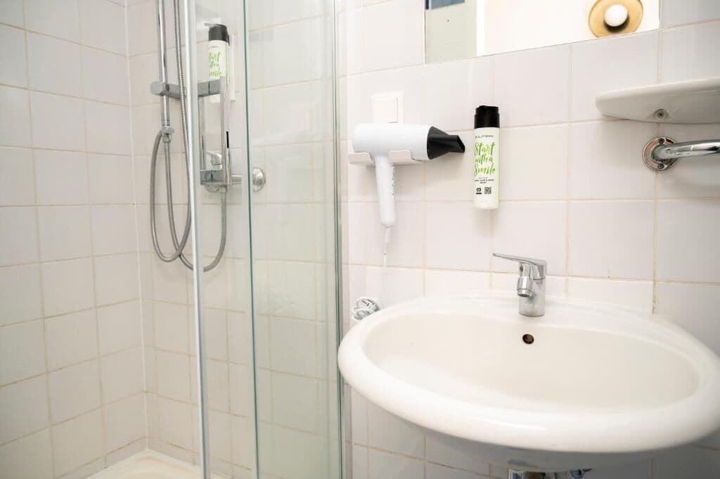 Ein Badezimmer mit Duschkabine aus Glas, einem weißen Waschbecken und einem an der Wand montierten Föhn.