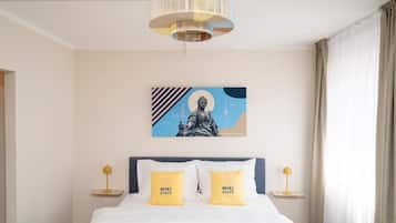 Ein Hotelzimmer mit einem Bett, zwei Nachttischlampen, einem Wandbild und einem Fenster mit Vorhängen.