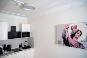A modern kitchen with white cabinetry, a black countertop, and a painting of a historical figure. - Miki Stays - 200m zum Prater (Vienna)