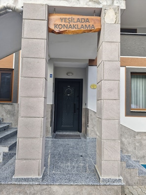 Entrada de un edificio con un letrero que dice 'YESILADA KONAKLAMA' y una puerta negra.