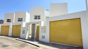 A row of modern buildings with garage doors, a stone wall entrance, and a clear sky. - Nerja Paradise Rentals - Villa La Marea (Nerja)