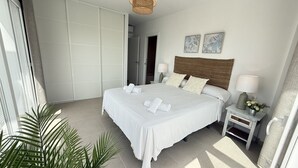 A hotel room with a bed, two bedside tables, a nightstand, a lamp, a wall-mounted artwork, and a door. - Nerja Paradise Rentals - Villa Barranco (Nerja)