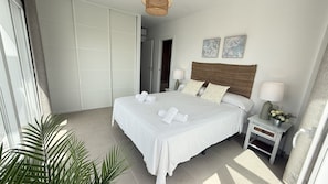 A hotel room with a bed, two bedside tables, a nightstand, a lamp, a wall-mounted artwork, and a door. - Nerja Paradise Rentals - Villa Barranco (Nerja)