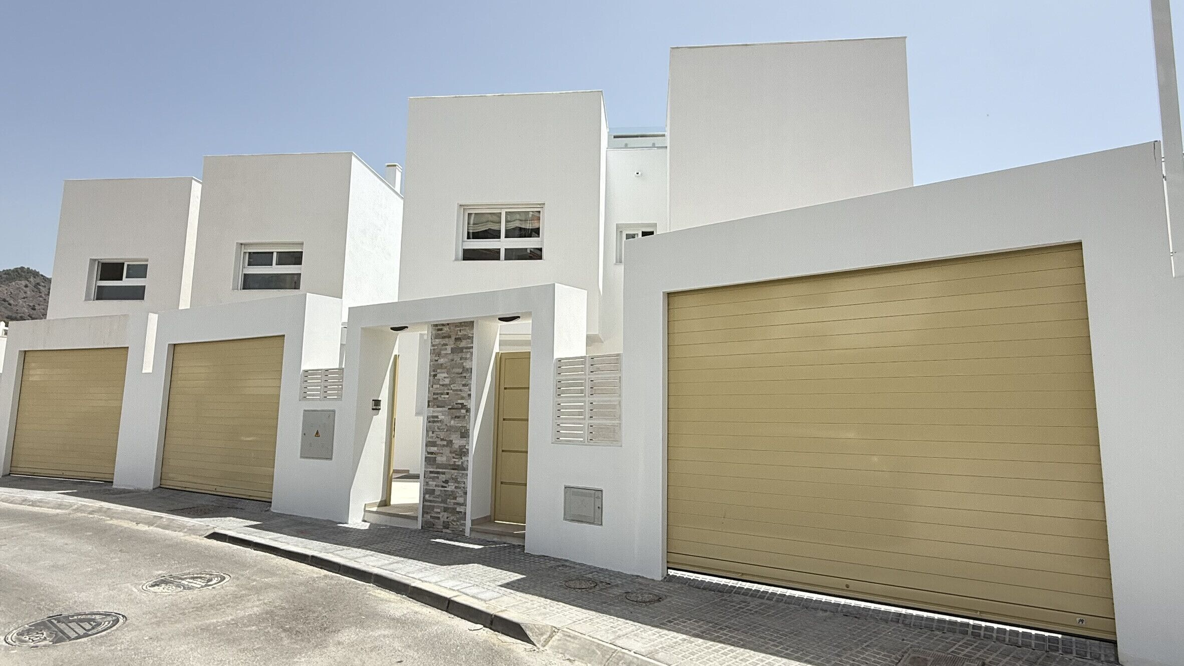 A row of modern buildings with garage doors, a stone wall entrance, and a clear sky.
