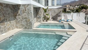 A swimming pool with stone walls and a view of a mountainous town. - Nerja Paradise Rentals - Villa Barranco (Nerja)