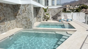 A swimming pool with stone walls and a view of a mountainous town. - Nerja Paradise Rentals - Villa Barranco (Nerja)