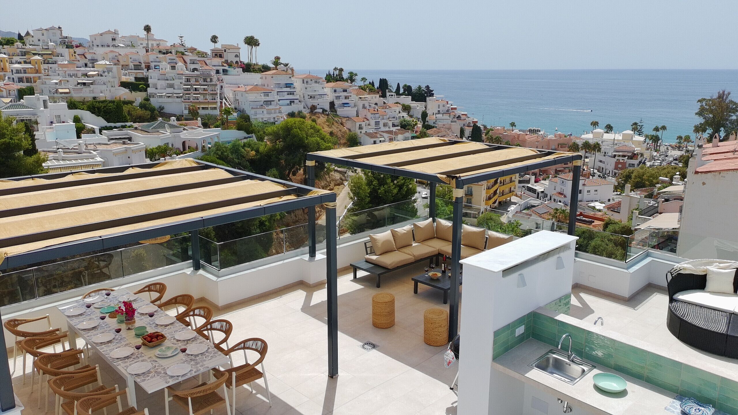 A rooftop terrace with a dining area, outdoor seating, and a view of the sea and cityscape.