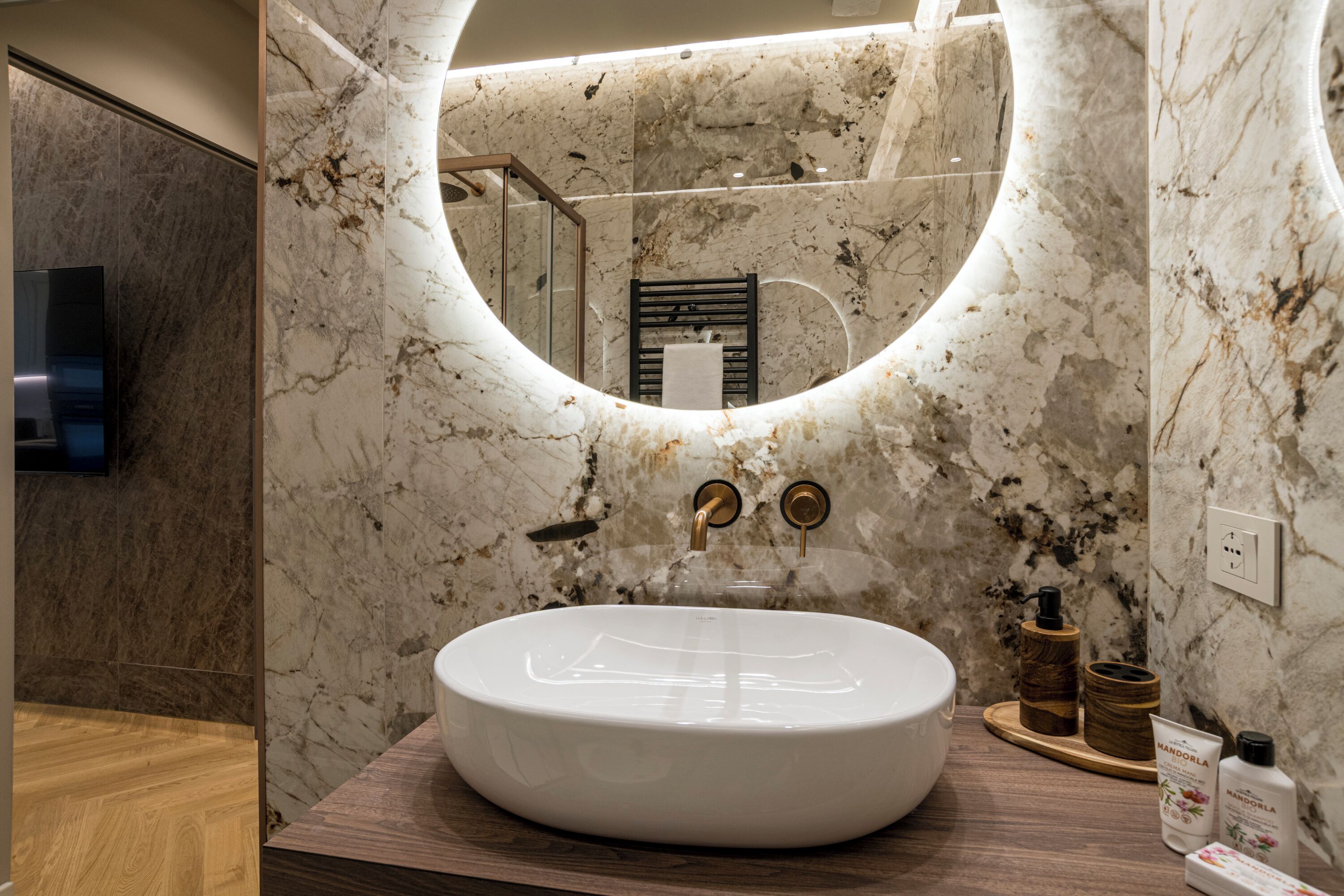 A bathroom with a large oval sink, a round mirror, and a wooden vanity.