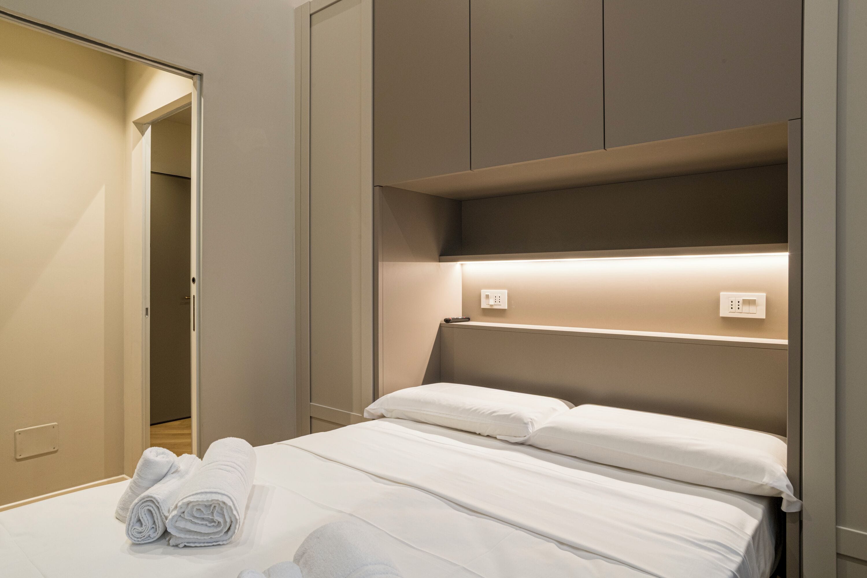 A hotel room with a bed, a closet, and a shelf unit.