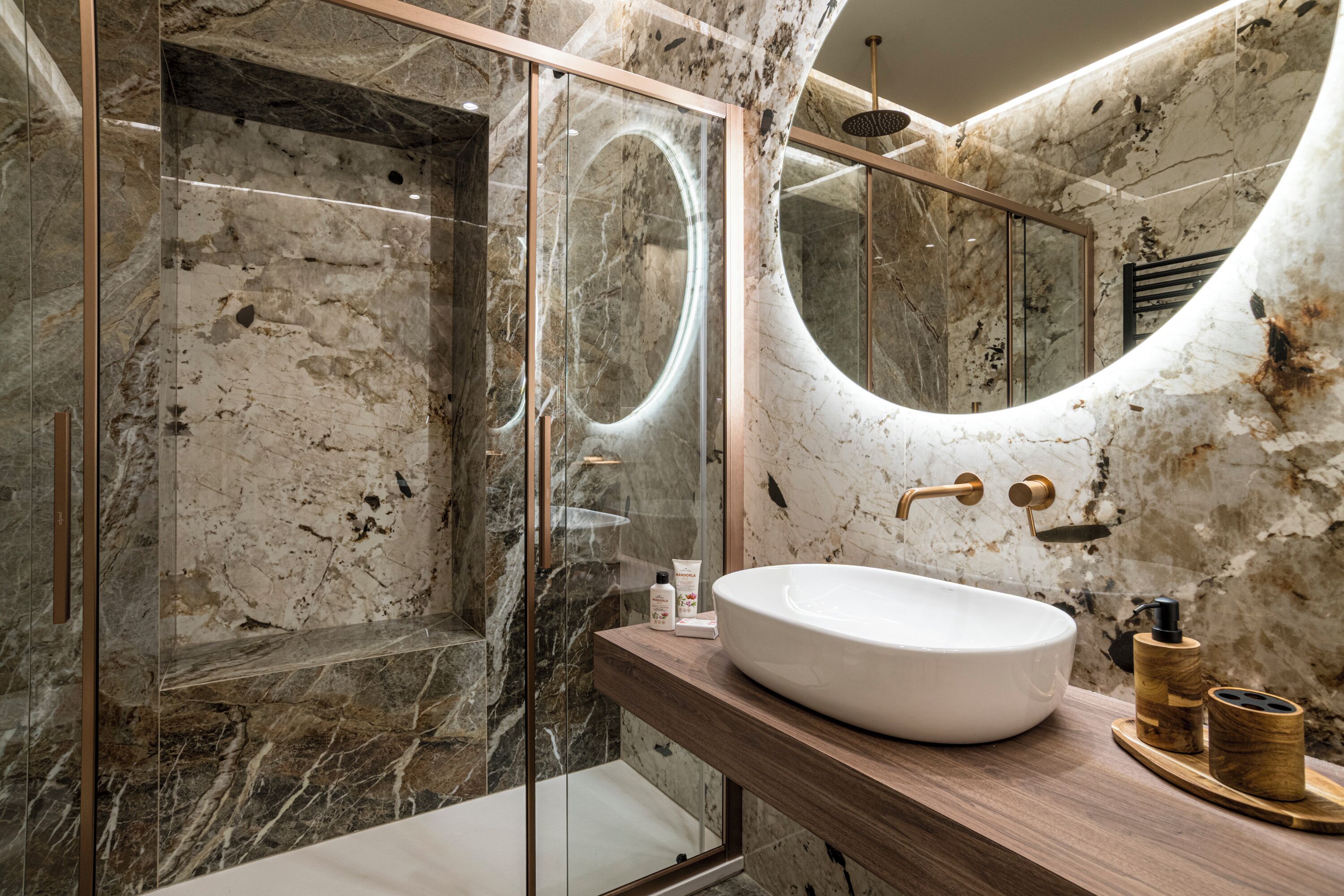 A bathroom with a marble wall, a glass-enclosed shower, and a wooden vanity with a white sink.
