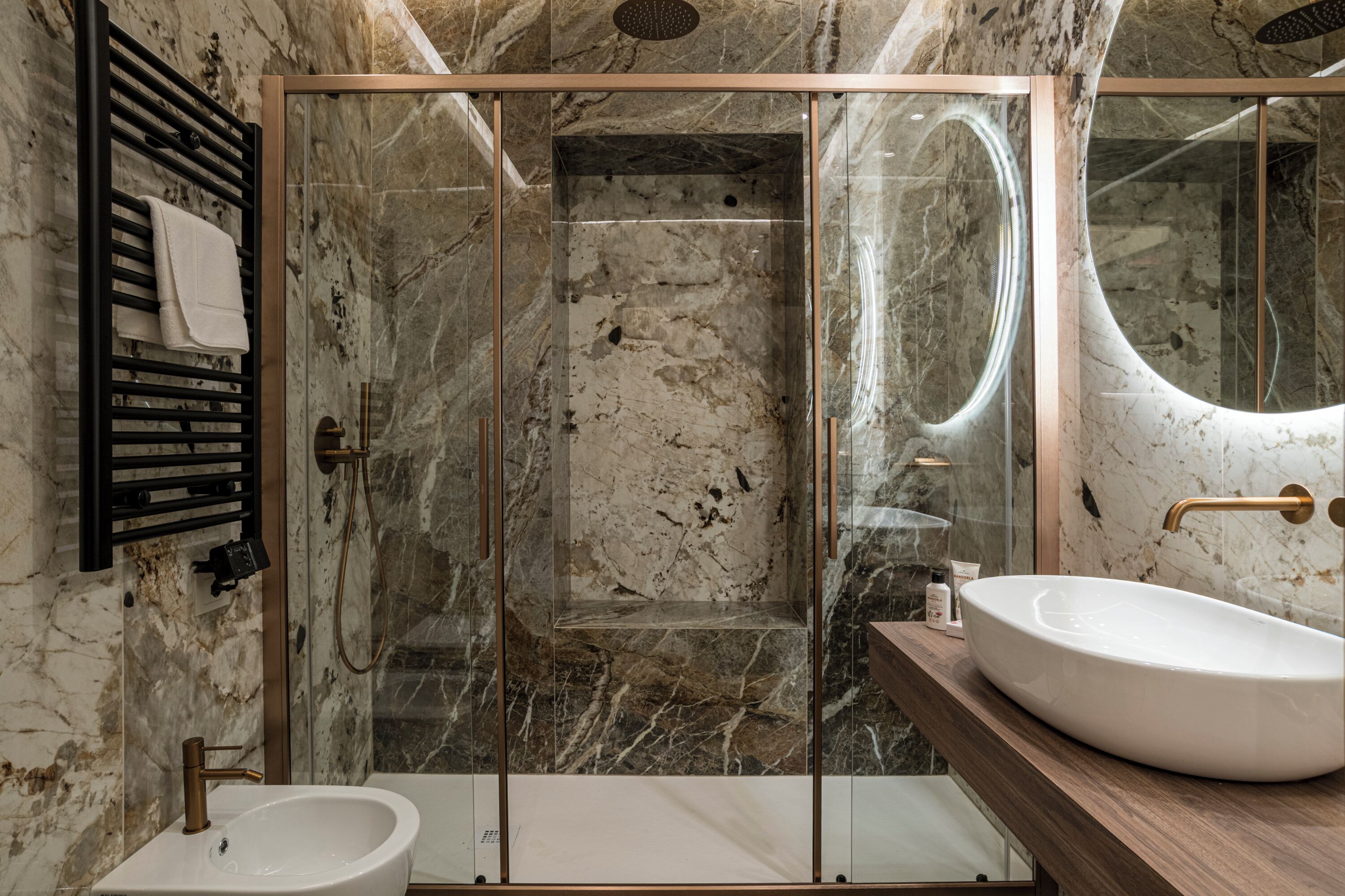 Une salle de bain moderne avec une douche en verre, un lavabo blanc et un mur recouvert de carreaux de marbre.