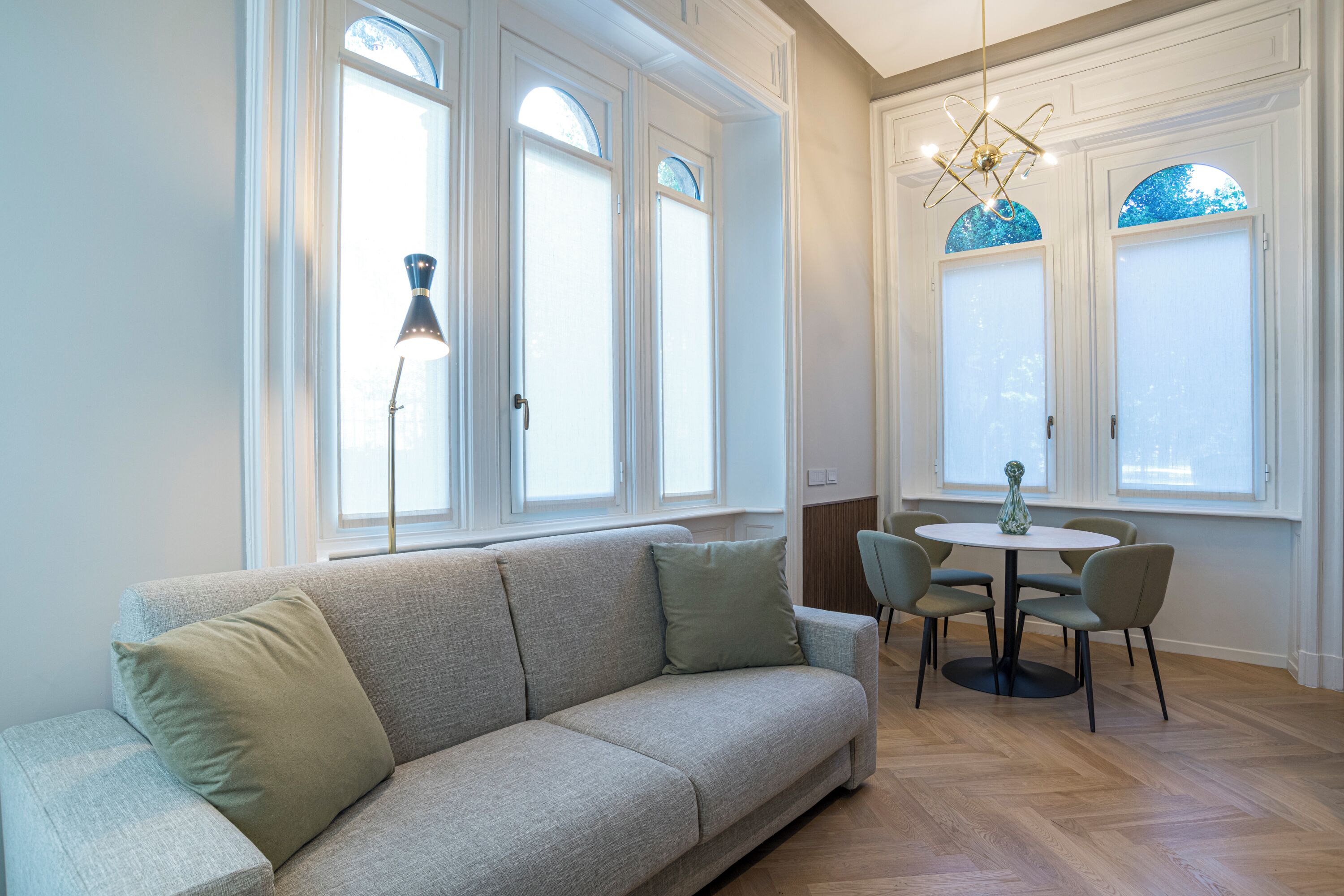 Ein modernes Wohnzimmer mit einer Couch, einem Esstisch mit Stühlen und großen Fenstern mit dekorativen Glasverzierungen.