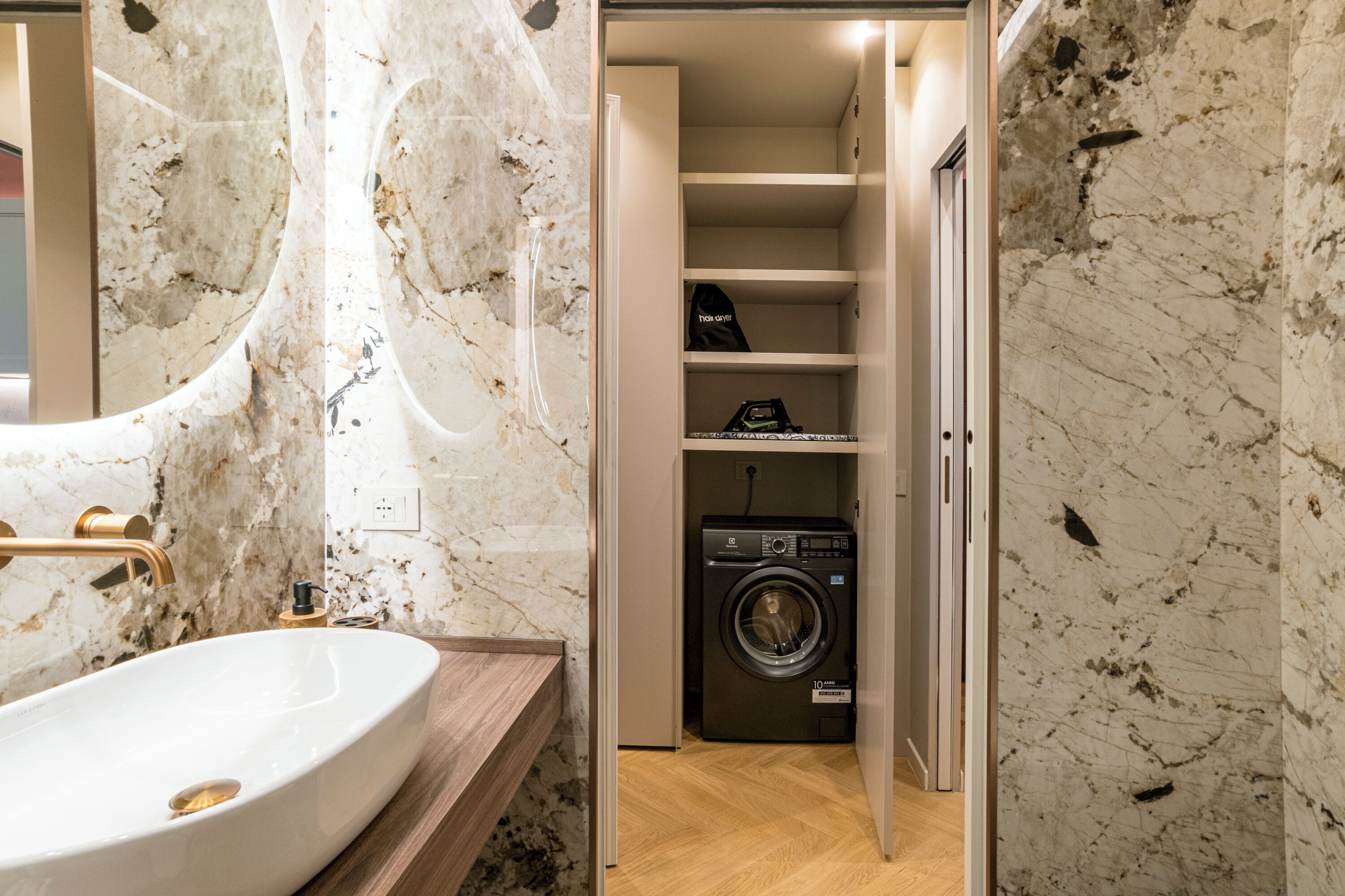 A bathroom with a marble sink, a built-in washing machine, and a wooden vanity.
