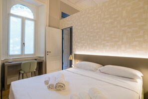 Une chambre d’hôtel avec un lit, un bureau, une chaise et une fenêtre.