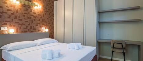 Una habitación de hotel con cama, lámparas de noche, armario, escritorio y una silla.
