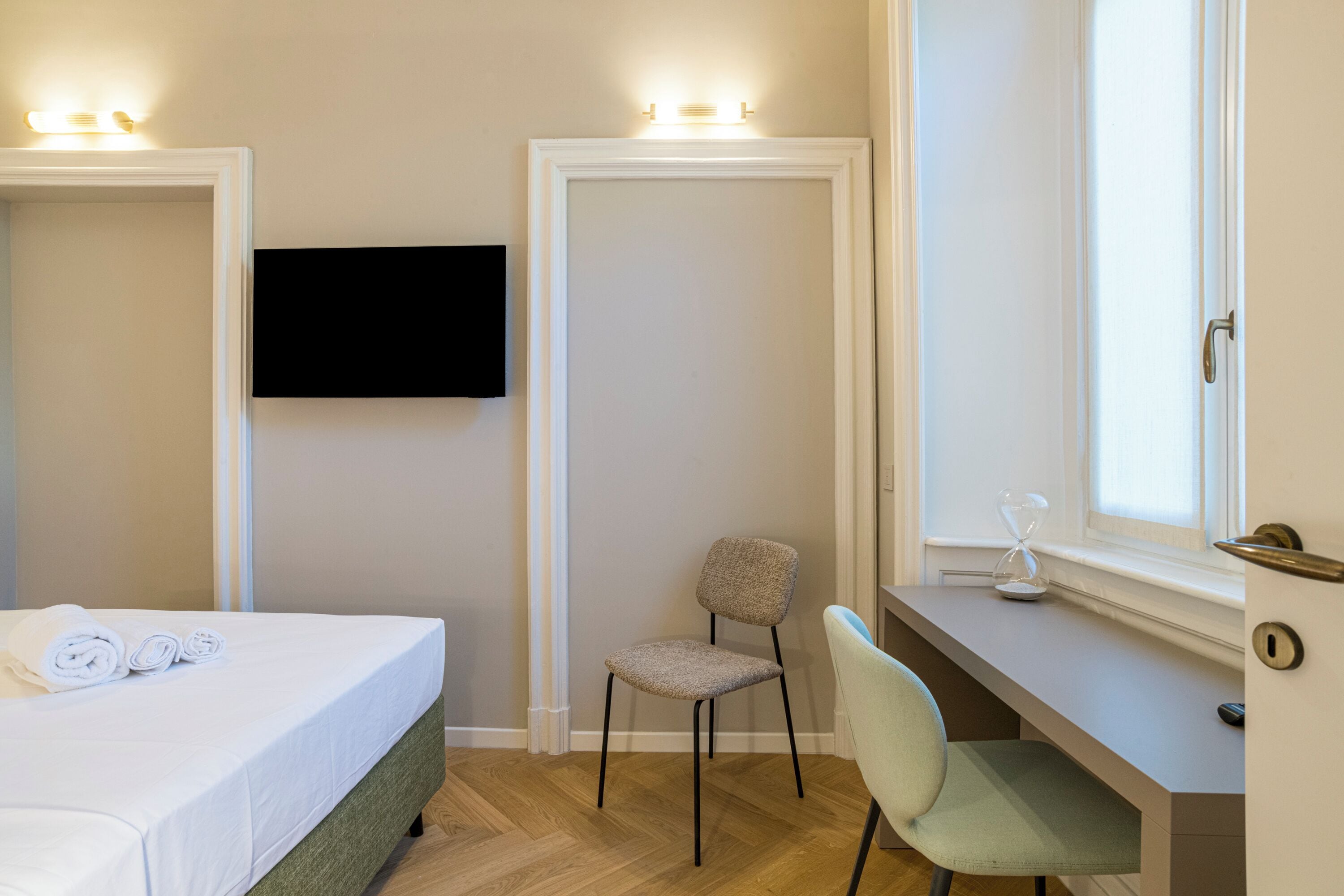 Una habitación de hotel con cama, escritorio, silla, televisor y ventana.