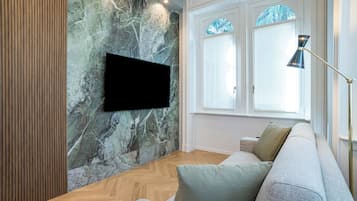 Moderni olohuone, jossa on seinään kiinnitetty litteänäyttöinen televisio, marmoriseinä, puulattia, harmaa sohva koristetyynyineen ja lattiavalaisin.