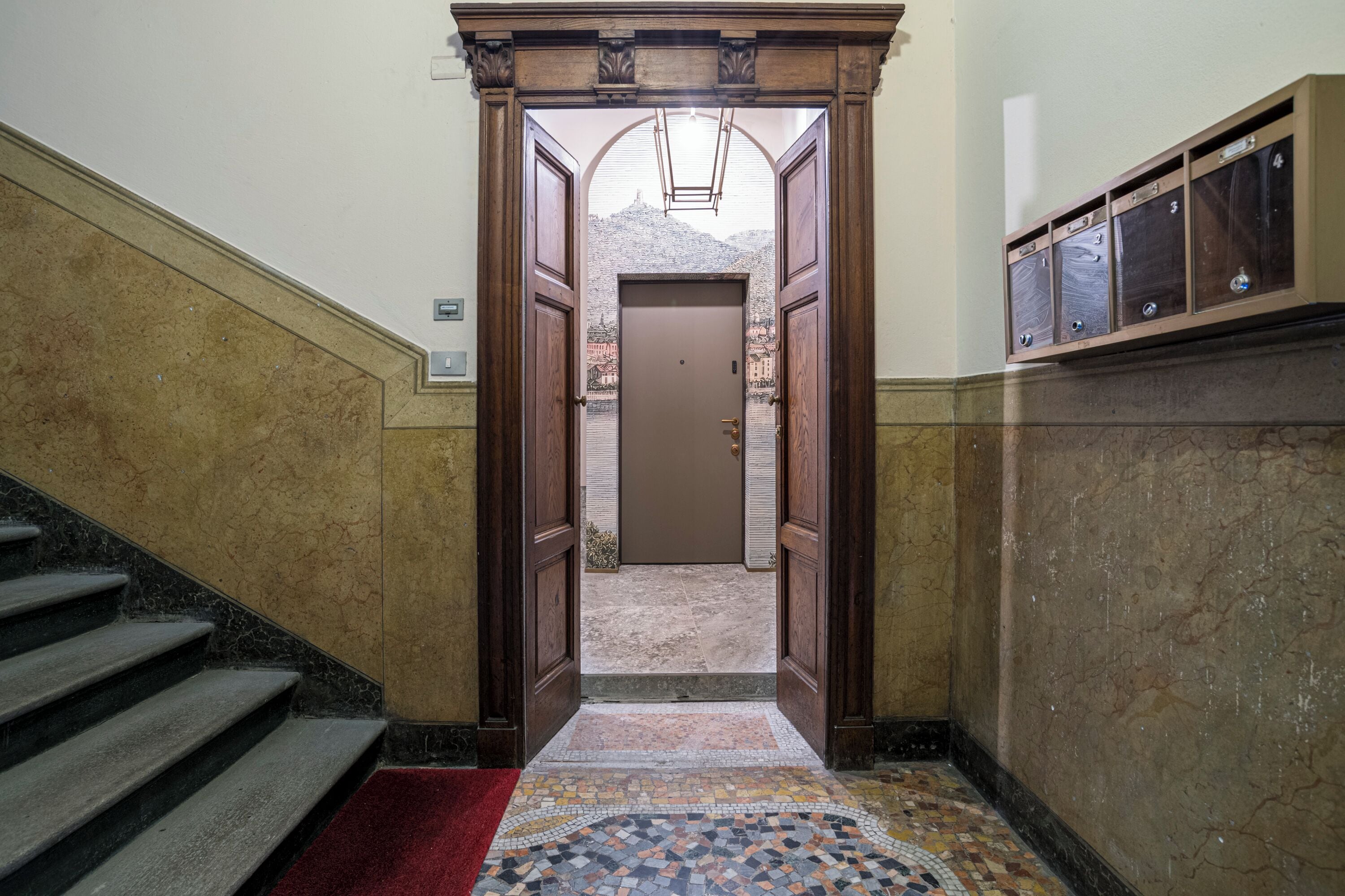 Un corridoio con una porta in legno, un pavimento piastrellato e una scala a sinistra.