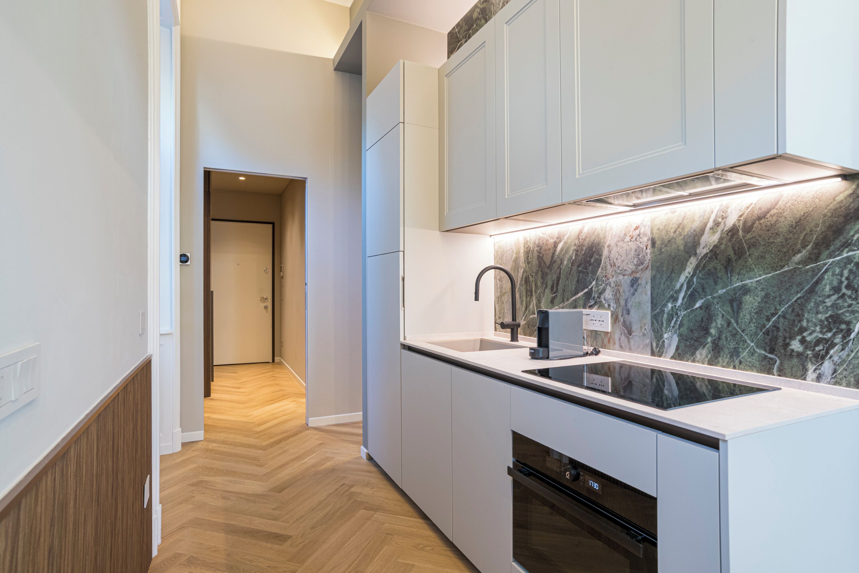 Una cucina moderna con forno a incasso, zoccolo di marmo e pavimento in assi di legno.