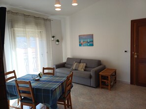A living room with a sofa, a dining table with chairs, a painting on the wall, and a door. - Laura's House (Palermo)