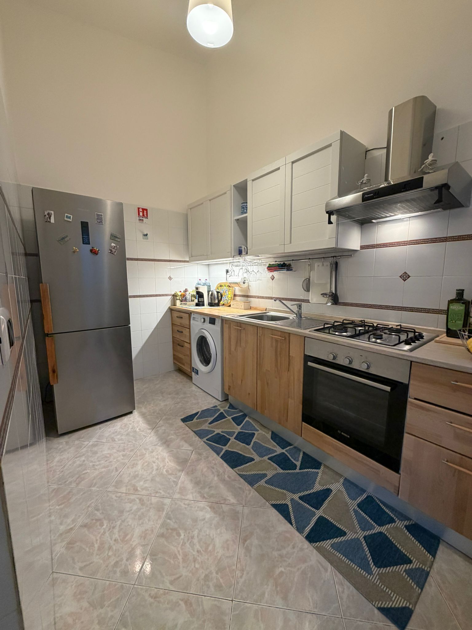 Een moderne keuken met een roestvrijstalen koelkast, een ingebouwde wasmachine, een gasfornuis en houten keukenkastjes.