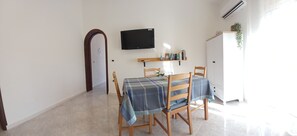A dining area with a table set for four, a flat-screen TV mounted on the wall, and a bookshelf with books and decorative items. - Laura's House (Palermo)