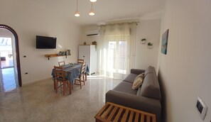 A living room with a sofa, a dining table with chairs, a TV mounted on the wall, and a window with curtains. - Laura's House (Palermo)