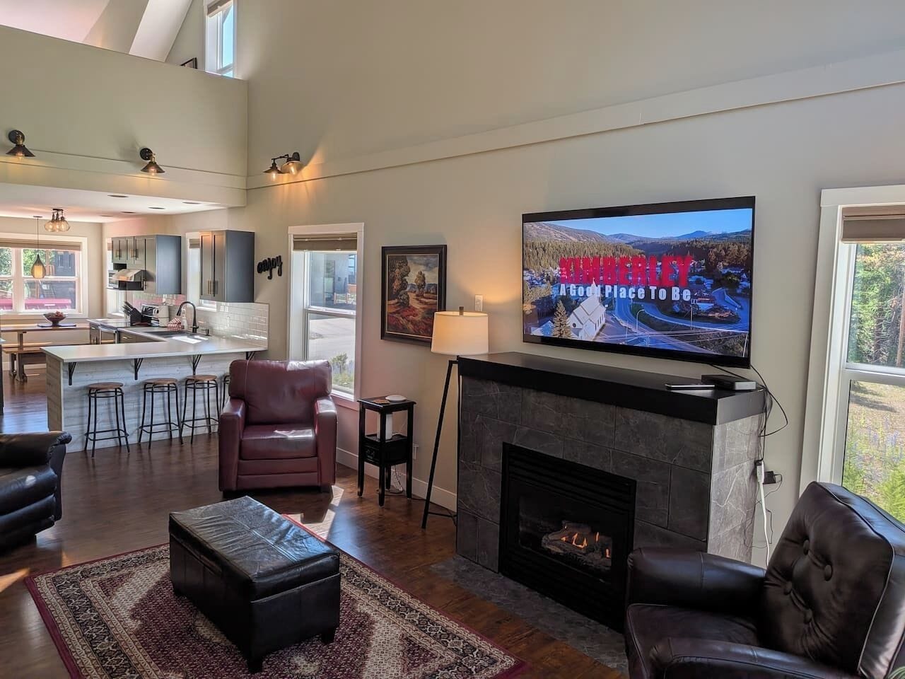 Ein modernes Wohnzimmer mit Kamin, einem darüber montierten Fernseher und einer Küche im Hintergrund.