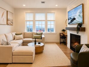 Ein modernes Wohnzimmer mit einer Eckcouch, einem runden Couchtisch, einem Kamin und einem großen, an der Wand befestigten Fernseher.