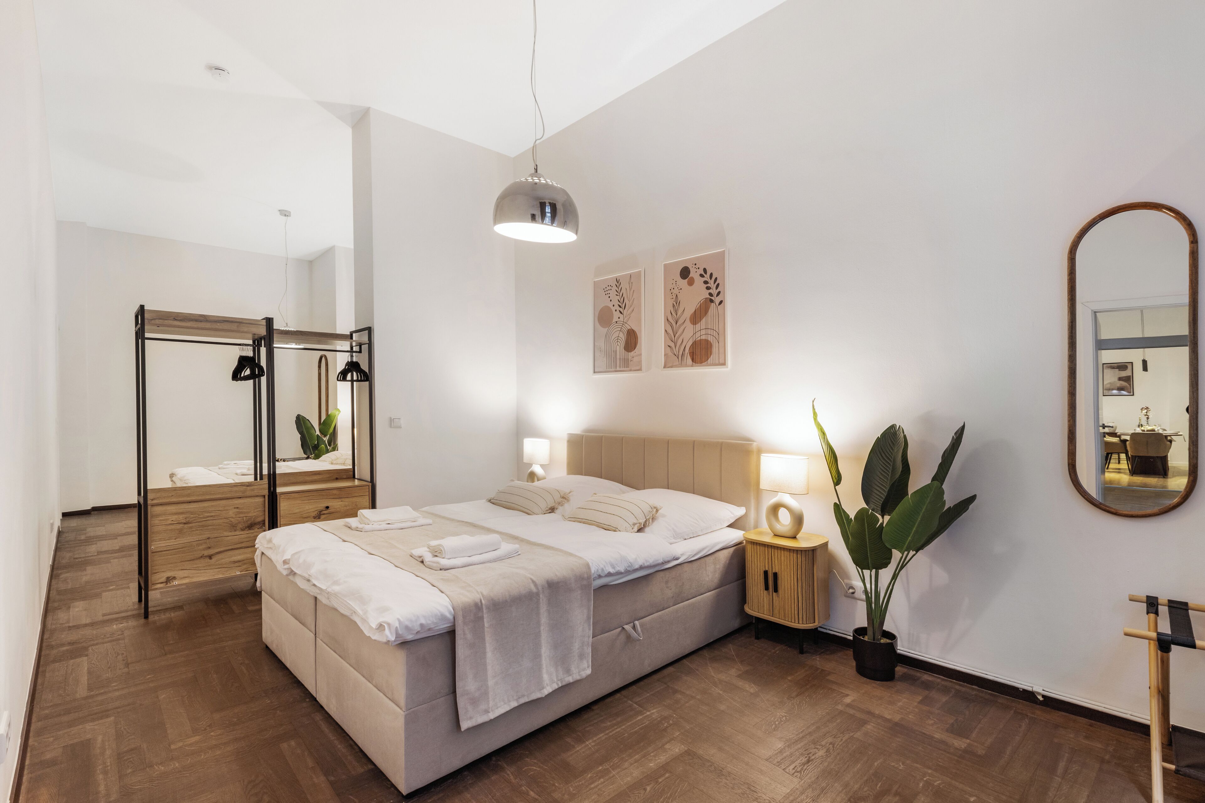 A modern bedroom with a bed, bedside lamps, a mirror, and artwork on the wall.