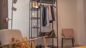 A modern room with a black metal shelving unit containing books, a vase, and a handbag. There is a chair with a cushion and a small table with a pink cloth.