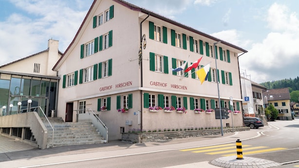 A building with a sign reading 'CASTHOF HIRSCHEN' and multiple flags.