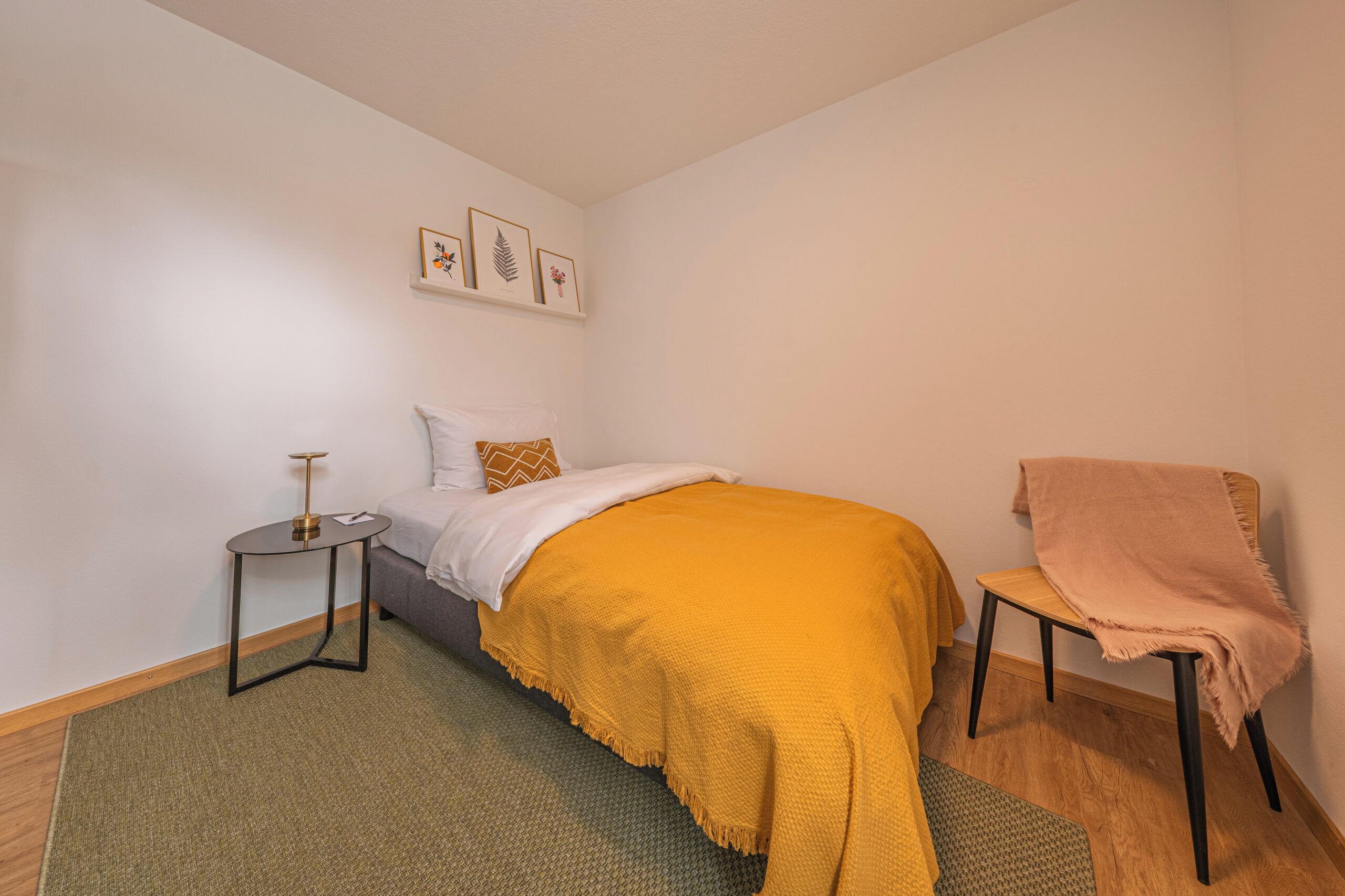 A bedroom with a bed, a bedside table, a chair, a rug, and wall art.