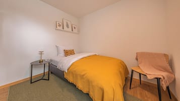 A bedroom with a bed, a bedside table, a chair, a rug, and wall art.