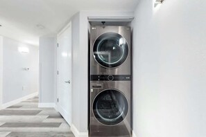 A laundry room with two front-loading washing machines, a door, and a hallway with a patterned floor. - Carolinian Beach Resort 1230 (Myrtle Beach)