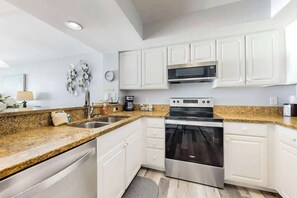 A modern kitchen with white cabinets, granite countertops, stainless steel appliances, and a built-in oven. - Carolinian Beach Resort 1230 (Myrtle Beach)
