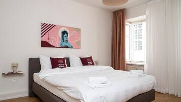 A neatly made bed with white linens and two pillows, a wall-mounted artwork, and a window with curtains.