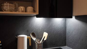 Una cocina con un refrigerador negro, un hervidor, una cafetera y un juego de utensilios sobre la encimera.
