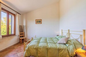 Une chambre à coucher avec un lit, une fenêtre, un tableau au mur et une chaise agrémentée de plantes.