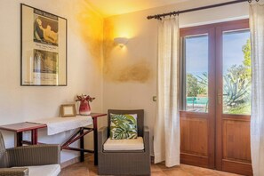 Ein Zimmer mit Korbsessel, kleinem Tisch, gerahmtem Bild und einem Poster an der Wand.