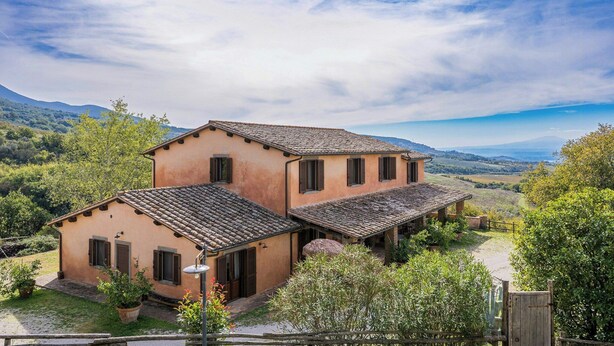 A two-story building with a tiled roof, surrounded by greenery and a mountainous backdrop. - Farmhouse with pool between Orvieto and Todi (Montecchio)